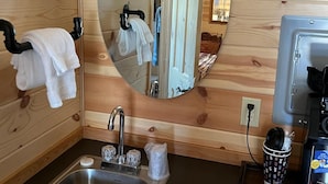 A wooden cabin bathroom with a sink, mirror, towel rack, and a small window. - The Gold Mine Hotel (Idaho City)