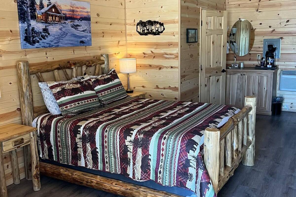 A cozy log cabin bedroom with a wooden bed, a nightstand, a dresser, and a mirror.