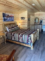 Un dormitorio rústico de cabaña con cama de madera, mesita de noche, cómoda y espejo.