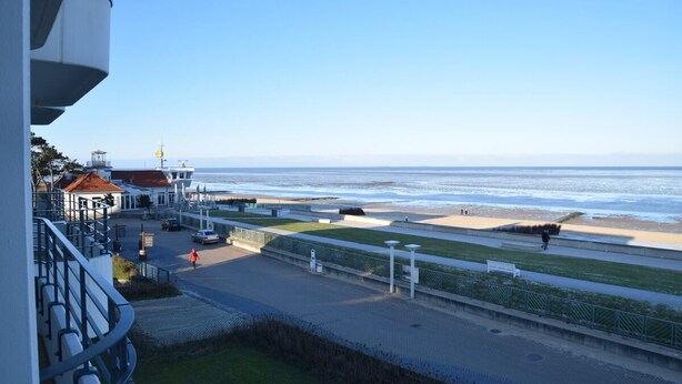 A coastal promenade with a clear view of the sea, a pedestrian path, and a building with a red roof. - Nautilus, Ferienwohnung 23 (Cuxhaven)