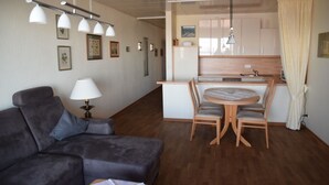 A compact living space with a sofa, a dining table with chairs, a kitchenette, and a ceiling light fixture. - Nautilus, Ferienwohnung 23 (Cuxhaven)