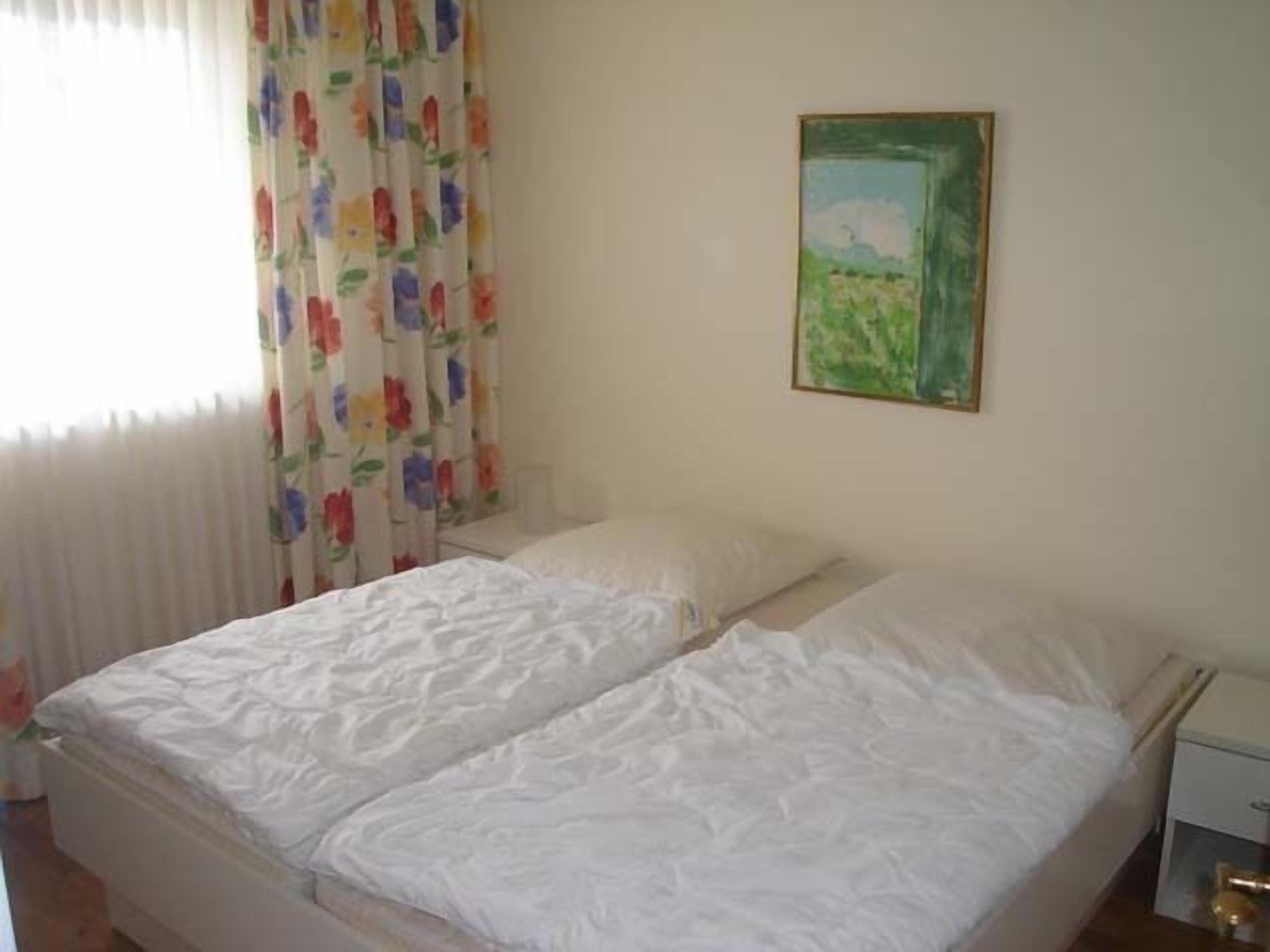 Een tweepersoonsbed met witte beddengoed in een kamer met een effen muur en een schilderij.