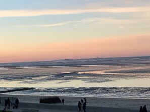 Eine Strandansicht mit Menschen, die am Ufer entlanggehen, ruhigem Meer und blauem Himmel.