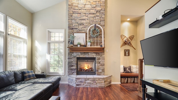 A living room with a stone fireplace, a black leather sofa, and a flat-screen TV. - MountainwoodMemories LkHarmony 5bedroom Pool Beach SkiResort Tennis (Lake Harmony)