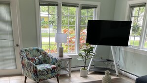 Ein Wohnzimmer mit Sofa, Sessel, Couchtisch, Fernseher und einer Topfpflanze.