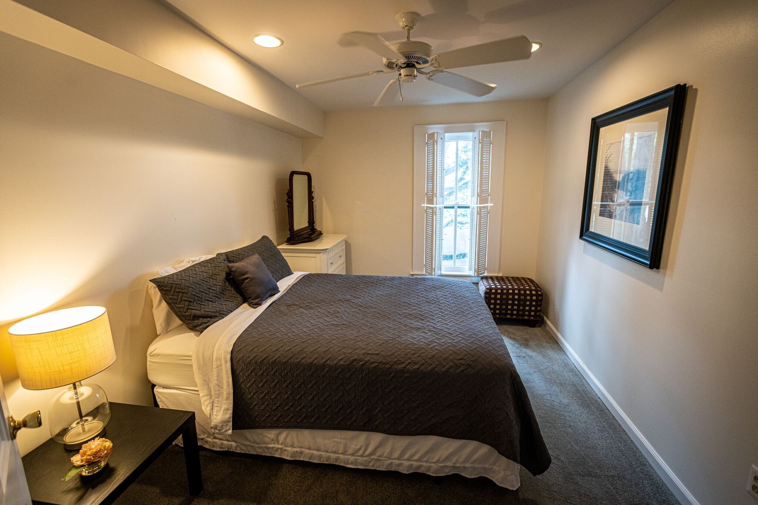 Une chambre à coucher avec un lit, une table de chevet, une lampe et un ventilateur de plafond.