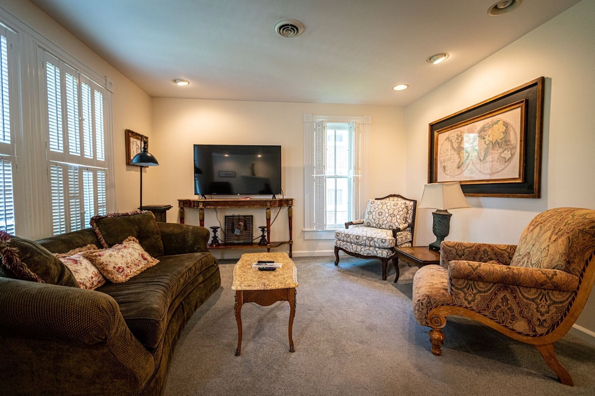 A living room with a sofa, armchairs, a coffee table, a TV, and a framed map on the wall.