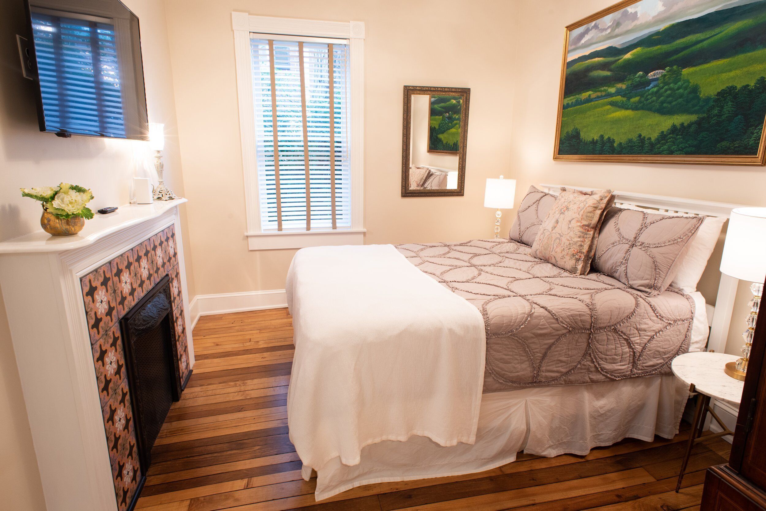 A bedroom with a bed, a fireplace, a television, and a painting on the wall.