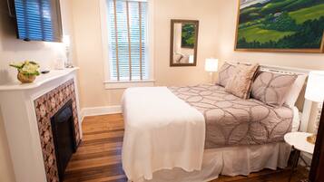 A bedroom with a bed, a fireplace, a television, and a painting on the wall.