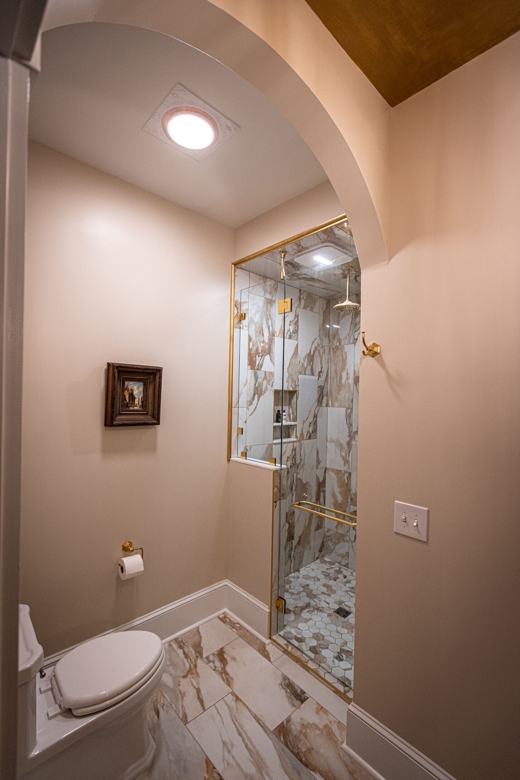 A bathroom with a toilet, marble flooring, a glass shower enclosure, and a framed picture on the wall.