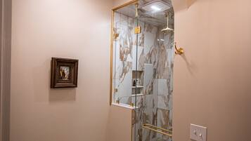 A bathroom with a toilet, marble flooring, a glass shower enclosure, and a framed picture on the wall.