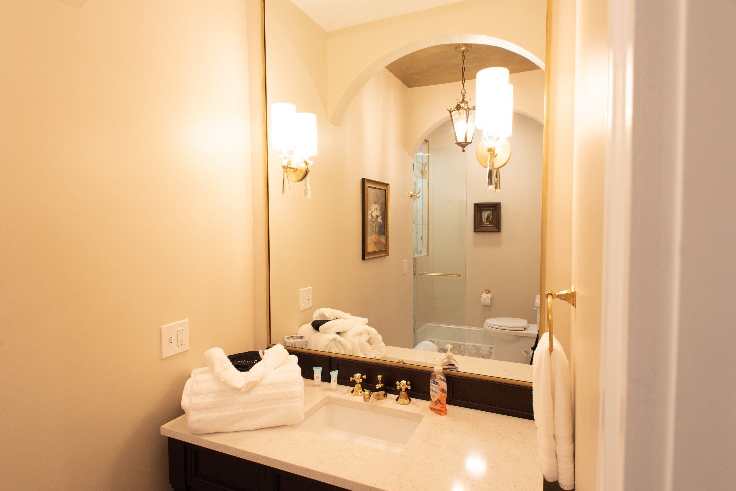 A bathroom with a large mirror, a sink, and a shower visible in the reflection.