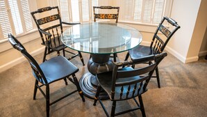 A round glass table surrounded by four chairs with wooden frames and cushioned seats. - Washington Street Quarters (Lewisburg)