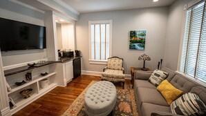A living room with a flat-screen TV, a sofa, an ottoman, and a patterned rug. - Washington Street Quarters (Lewisburg)