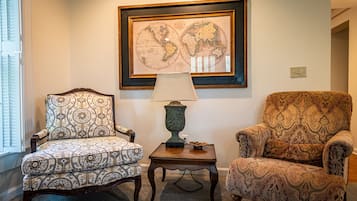 Una habitación con dos sillones estampados, una mesita con lámpara y un mapa del mundo enmarcado en la pared.