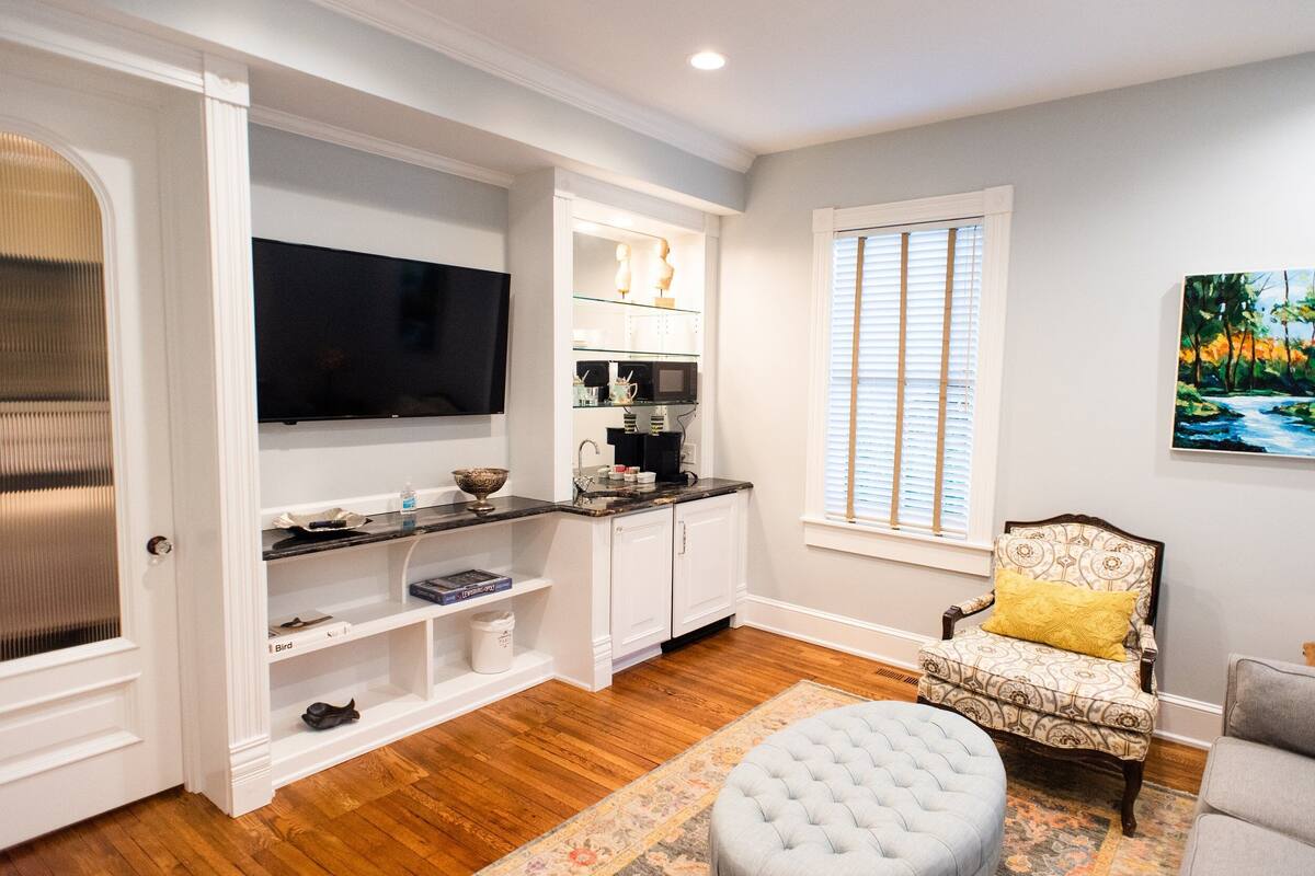 A modern living room with a flat-screen TV, built-in shelves, a coffee maker, and a comfortable armchair with a yellow pillow.