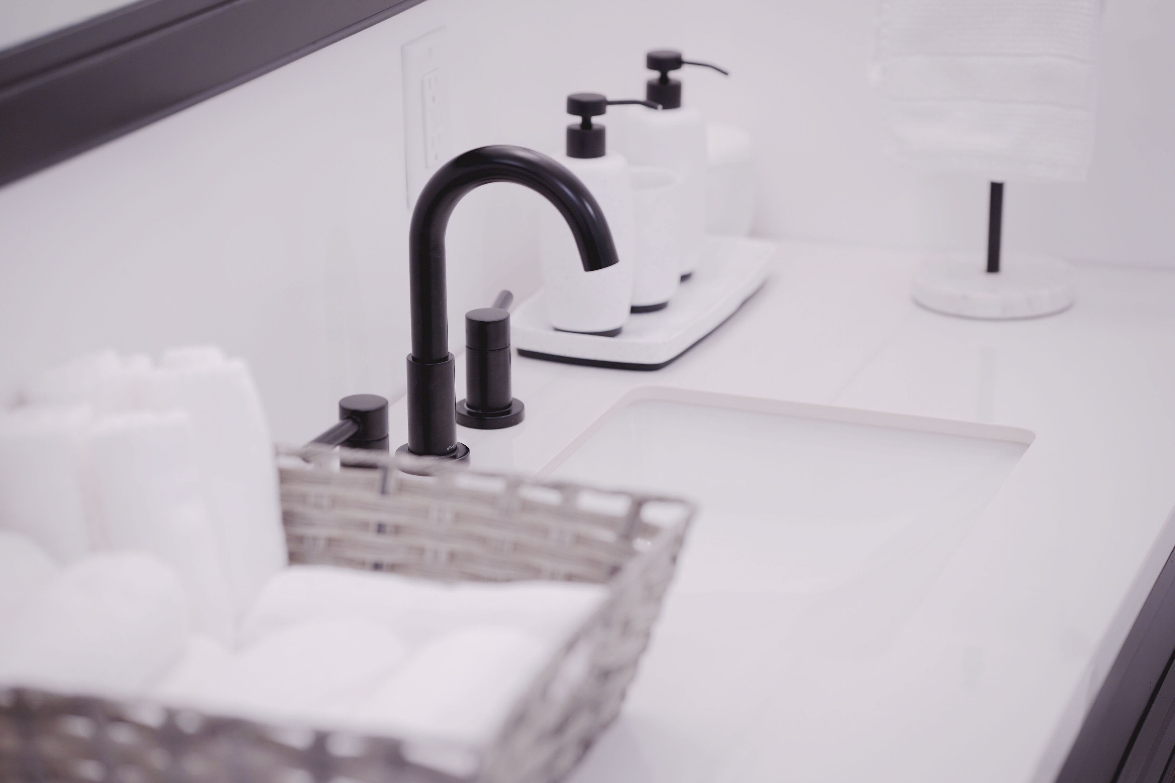 Un baño moderno con lavamanos blanco, grifo negro y dispensadores de jabón.