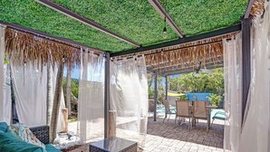 Un espacio de estar techado al aire libre con piscina al fondo.