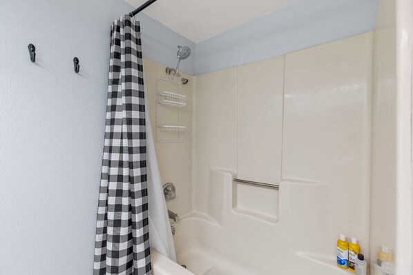 Un baño con ducha, una bañera blanca y una cortina de baño a cuadros.