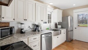 Una cocina moderna con armarios blancos, encimera de granito, lavavajillas, refrigerador y ventana con vistas a un parque.