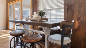 Una mesa de madera para comer con una bandeja, dos taburetes y una silla con asiento acolchado.
