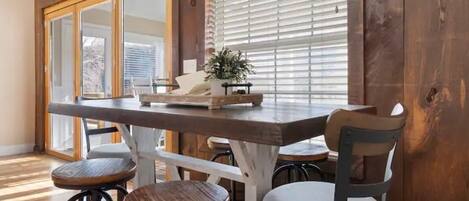 A wooden dining table with a tray, two stools, and a chair with a cushioned seat.
