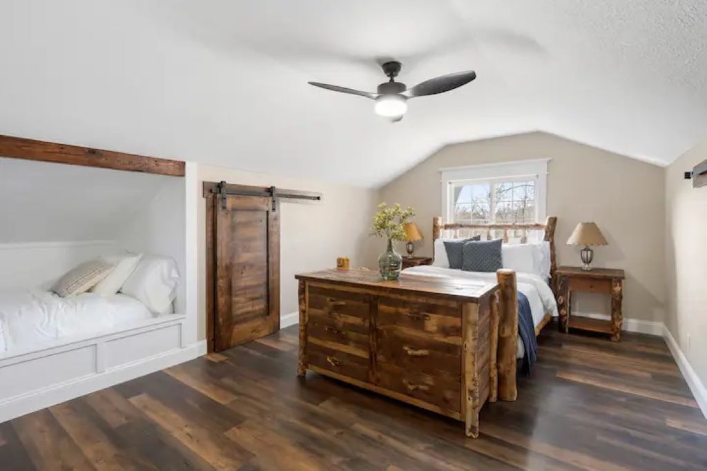 A bedroom with a loft bed, a wooden dresser, a ceiling fan, and a window with a view.