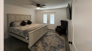 A bedroom with a bed, a ceiling fan, a door, and a chair.