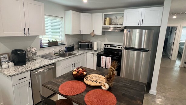 A modern kitchen with white cabinets, stainless steel appliances, and a central island with stools.