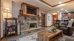 A cozy living room with a stone fireplace, wooden beams, a coffee table, and a sofa. - Premier 1 BD/1 BR condo ski in and out.  Gondola is right outside the condo. (Truckee)