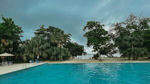 A swimming pool with clear blue water, surrounded by lush green trees and a sandy beach. - Negril Bungalow Paradise overlooking cliffs with Private Snorkeling Entrance. (Hanover Parish)
