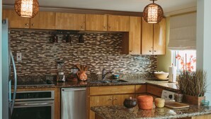A modern kitchen with wooden cabinets, a tiled backsplash, stainless steel appliances, and a granite countertop. - Negril Bungalow Paradise overlooking cliffs with Private Snorkeling Entrance. (Hanover Parish)