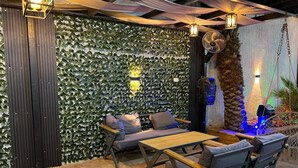 Un rincón interior acogedor con una pared cubierta de follaje verde, una mesa de madera y sillas con cojines.