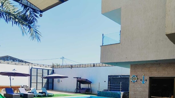 Piscina con sillas de descanso y una mesa, rodeada por un porche cubierto.