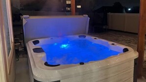 Un bain à remous doté d’un éclairage bleu, entouré d’une terrasse en bois et d’un espace couvert agrémenté de guirlandes lumineuses.