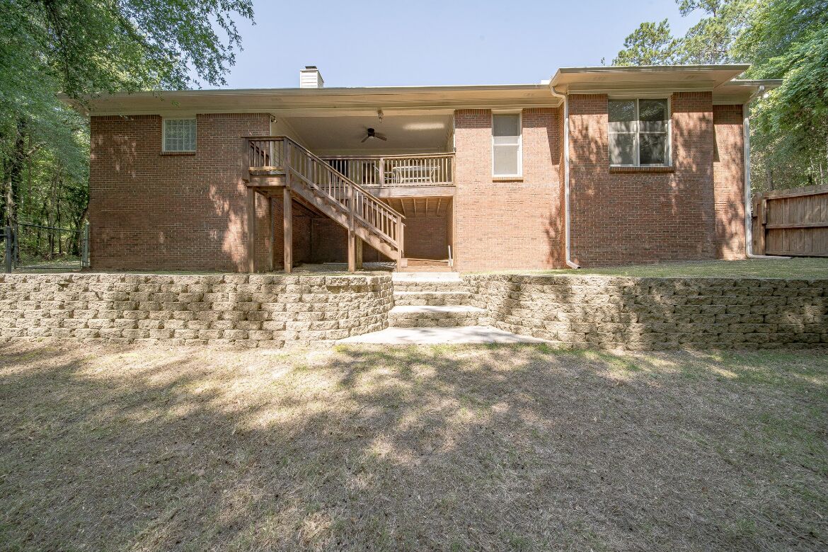 A two-story brick house with a front porch, a staircase leading to the upper level, and a fenced yard.