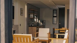 Un salon moderne avec des meubles en bois, un coin cuisine équipé d’un four à micro-ondes et une table à manger avec des chaises.