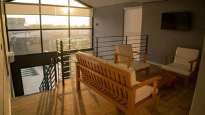 Un balcon spacieux agrémenté de meubles en bois, un téléviseur fixé au mur et une vue sur la ville grâce à de grandes fenêtres.