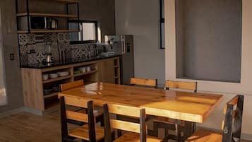 A compact kitchen with a wooden dining table and chairs, a built-in microwave, and a refrigerator.