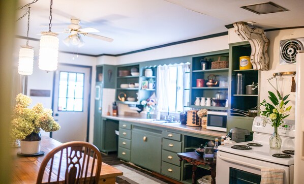 A kitchen with green cabinets, a wooden dining table, and a white stove.