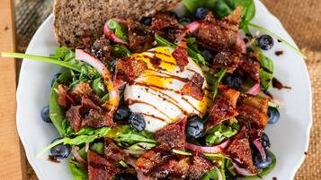 A salad with bacon, eggs, and blueberries on a white plate.