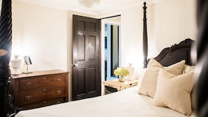 A four-poster bed with a dark headboard, a bedside table with a vase of flowers, and a wooden dresser with drawers.