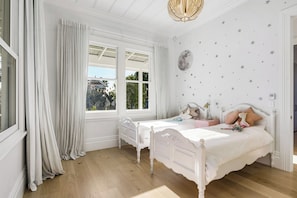 A bedroom with two beds, a window with curtains, a moon wall decal, and a chandelier.