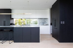 A modern kitchen with a central island, dark cabinetry, and a large window providing a view of greenery.