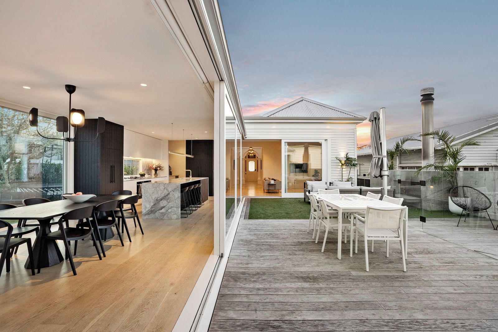 A modern kitchen with a marble island, a dining area with a wooden table and chairs, and a patio with a white table and chairs.