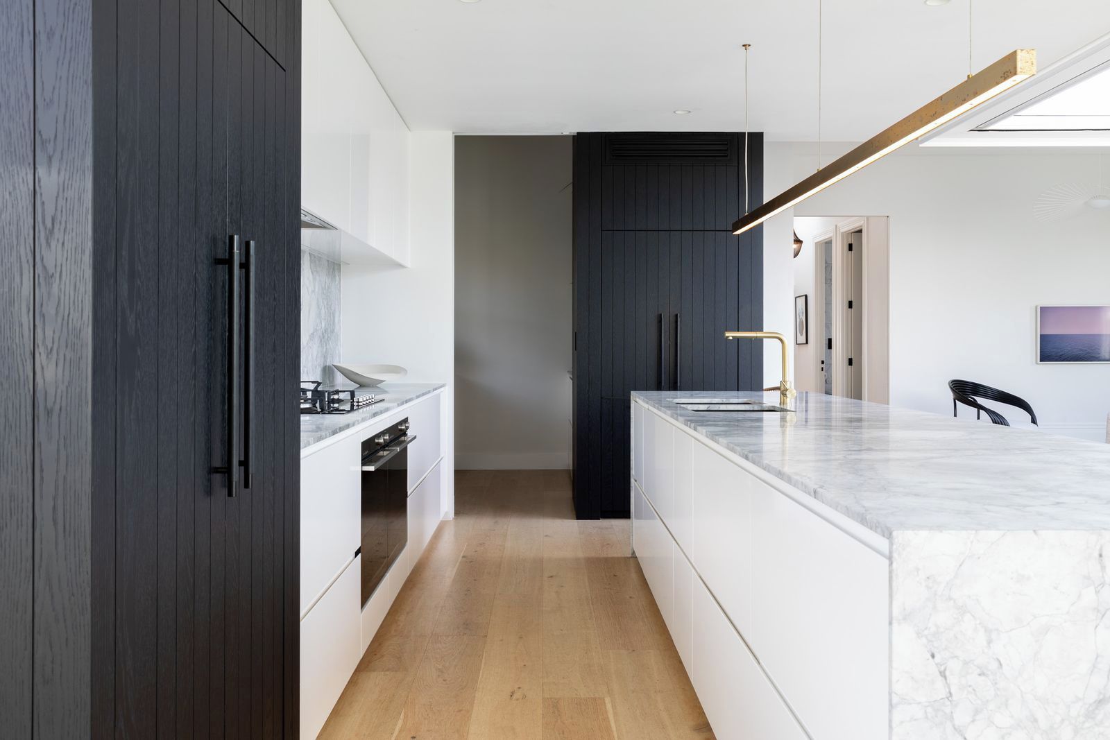 A modern kitchen with dark cabinetry, a marble countertop, and a pendant light.