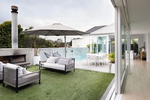 A modern outdoor living space with a barbecue, seating area, and a glass-enclosed pool.