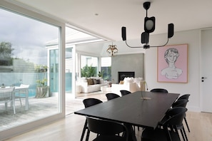 A modern dining area with a large table and chairs, a chandelier, and a view of the outdoor patio.
