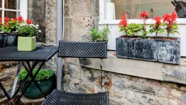Un bâtiment en pierre avec une fenêtre, une table entourée de chaises et des plantes en pot.