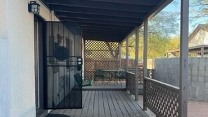 A covered outdoor area with a wooden deck, a metal railing, and a door leading to a garage. - Historic University 3BR  (Tucson)